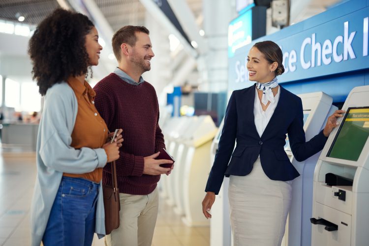 Woman, passenger assistant and couple at airport by self service check in station for information, help or FAQ. Portrait of happy female services agent helping travelers register or book air flight.